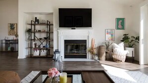 Una sala de estar con chimenea, un televisor montado encima y una estantería.