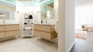 Un baño moderno con tocador blanco, estante empotrado con artículos de aseo y un espejo grande.