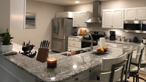 A modern kitchen with white cabinets, stainless steel appliances, a granite countertop, and a central island with seating. - The Mighty Oaks,Quiet,Hot Tub,Fire Pit,Cinema Room,Pool Table, 10 min to Town (Bar Harbor)