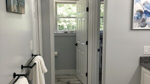 A hallway with a wooden floor, white walls, and a door leading to a bathroom. - The Mighty Oaks,Quiet,Hot Tub,Fire Pit,Cinema Room,Pool Table, 10 min to Town (Bar Harbor)