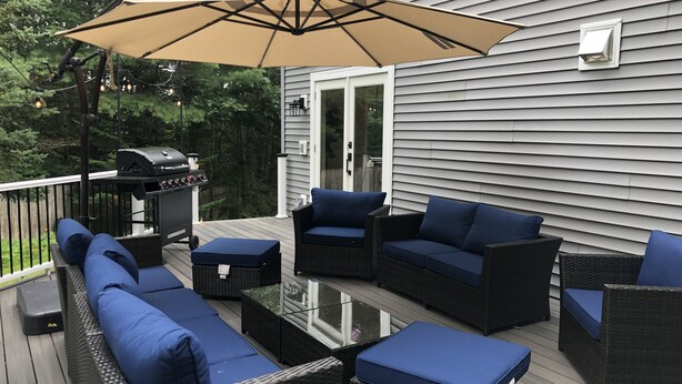 An outdoor deck with wicker furniture, a glass table, and a barbecue grill. - The Mighty Oaks,Quiet,Hot Tub,Fire Pit,Cinema Room,Pool Table, 10 min to Town (Bar Harbor)