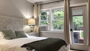 A bedroom with a bed, a nightstand, a lamp, a window with curtains, and a view of the outdoors. - The Mighty Oaks,Quiet,Hot Tub,Fire Pit,Cinema Room,Pool Table, 10 min to Town (Bar Harbor)
