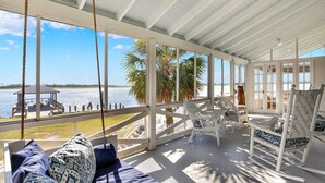 A covered outdoor area with a view of the water, white wicker furniture, and a swing. - Back River Views, Wraparound Porch, Dock (Tybee Island)