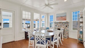 A dining area with a round table, white chairs, and a ceiling fan. - Back River Views, Wraparound Porch, Dock (Tybee Island)