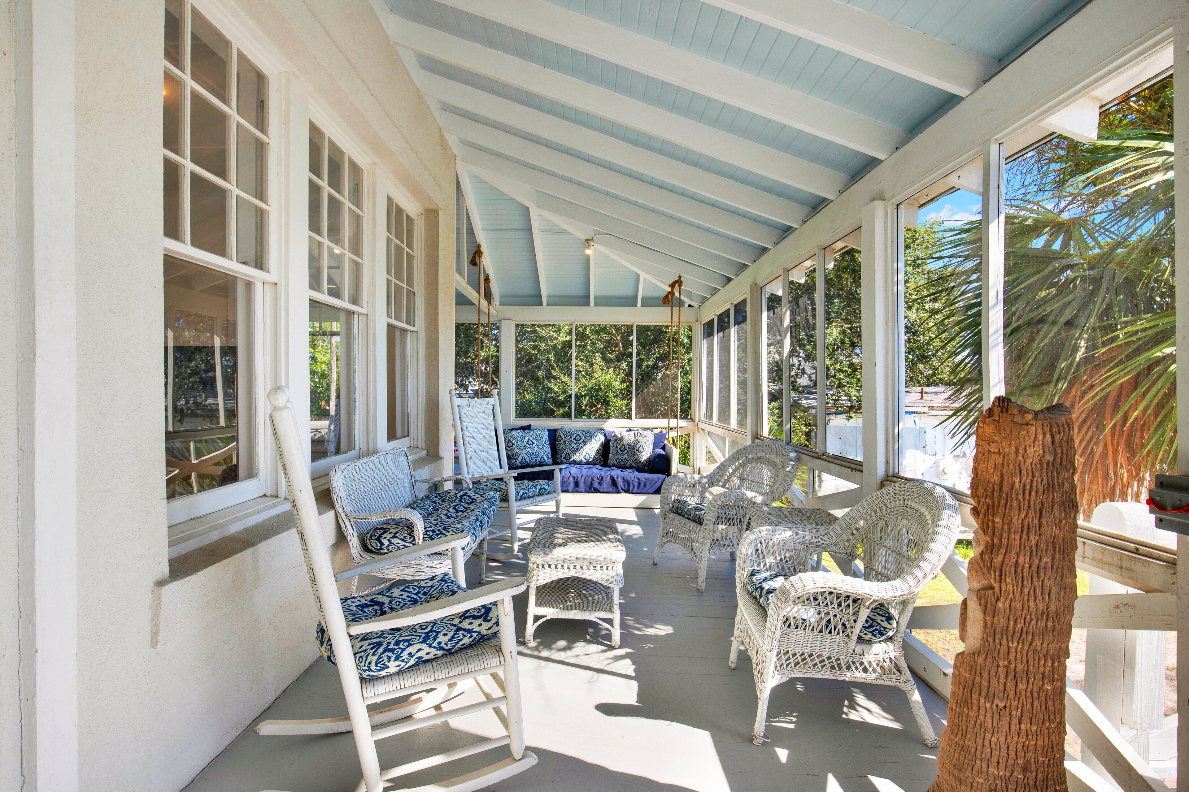 Eine überdachte Veranda mit Korbmöbeln, einem blauen Sofa und einem Holzstamm.