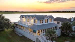 A waterfront house with a large deck, multiple windows, and a staircase leading to the upper level. - Back River Views, Wraparound Porch, Dock (Tybee Island)