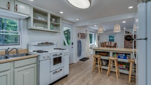 Una cocina moderna con gabinetes blancos, estufa a gas, lavamanos y taburetes de madera.