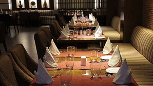 A restaurant with long tables set for dining, cushioned seating, and a modern interior design. - Cama Hotel (Mohali)