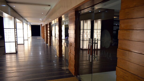 A corridor with wooden paneling, glass doors, and a reflective floor. - Cama Hotel (Mohali)
