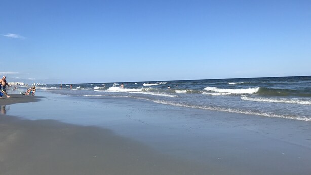 A beach with people swimming and walking along the shore.