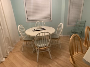 Uma área de refeições com uma mesa redonda, cadeiras brancas e piso de madeira.