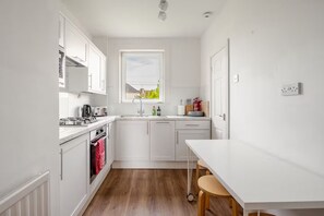A compact kitchen with white cabinets, a sink, a window, and a table with chairs. - Central St Andrews Apartment | The Open 2027 | Walk to Old Course (St Andrews)