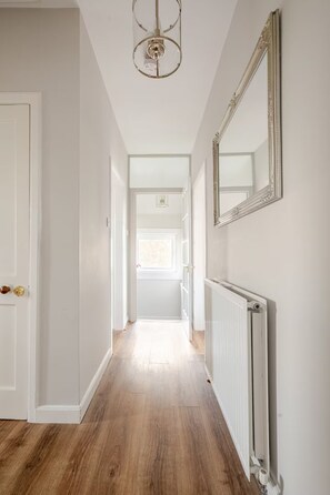 A hallway with a radiator, a door, and a mirror on the wall. - Central St Andrews Apartment | The Open 2027 | Walk to Old Course (St Andrews)