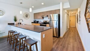 Una cocina moderna con una isla central, taburetes de madera, electrodomésticos de acero inoxidable y piso de madera.
