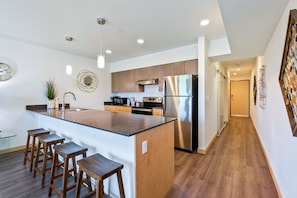 Una cocina moderna con una isla central, taburetes de madera, electrodomésticos de acero inoxidable y piso de madera.