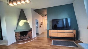 A modern living room with a fireplace, wooden flooring, a TV on a wooden cabinet, and a hallway leading to another room.