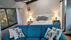 Una camera da letto con un letto, due comodini, un divano blu e una finestra con tende.