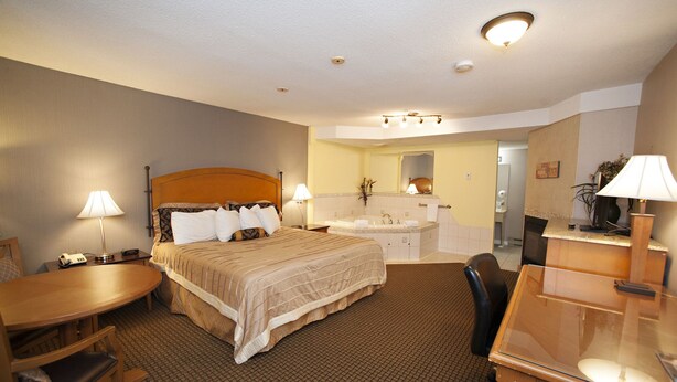 A hotel room with a bed, desk, chair, and a bathroom with a sink and mirror. - OYO First Canada Hotel Cornwall Hwy 401 ON (Cornwall)