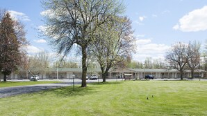 A motel with multiple rooms, a grassy lawn, and trees. - OYO First Canada Hotel Cornwall Hwy 401 ON (Cornwall)