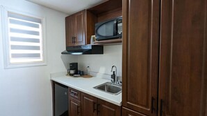 A compact kitchen with wooden cabinets, a microwave, a coffee maker, and a dishwasher. - OYO First Canada Hotel Cornwall Hwy 401 ON (Cornwall)