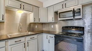 A kitchen with white cabinets, a stainless steel sink, a black stove, and a microwave. - Comfy, contemporary, quiet retreat with views of the Petroglyphs  (Albuquerque)
