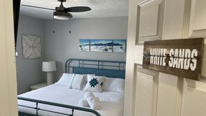 A bedroom with a bed, a ceiling fan, a nightstand, a lamp, and a wall-mounted sign. - Comfy, contemporary, quiet retreat with views of the Petroglyphs  (Albuquerque)