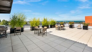 Une terrasse sur le toit, aménagée avec des espaces de détente en plein air, des plantes en pot et offrant une vue sur le panorama urbain.