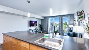 Une cuisine moderne dotée d’un grand îlot central, d’un évier en acier inoxydable et d’un téléviseur à écran plat fixé au mur.