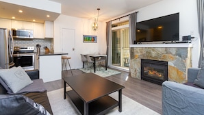 A modern living room with a fireplace, a dining area, and a kitchen with built-in appliances.
