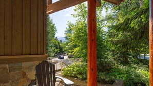A wooden deck with a stone wall, a wooden chair, and a view of a road with cars and trees.