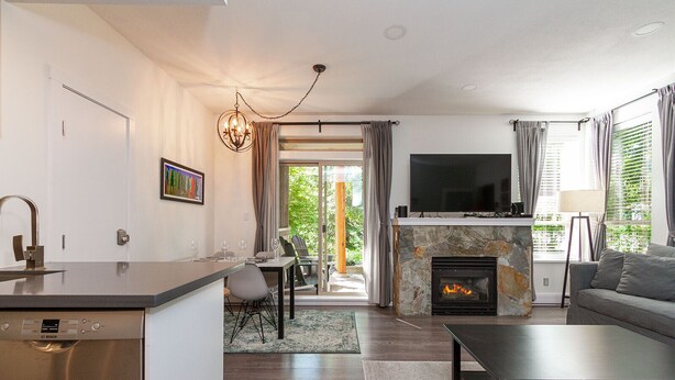 A modern living room with a stone fireplace, a flat-screen TV, and a dining area with a kitchen island.