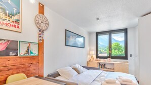 A hotel room with a bed, bedside table, and a window with a mountain view. - Appartement Courmayeur - Welkeys (Chamonix-Mont-Blanc)