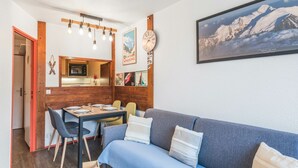 A cozy living room with a blue sofa, a dining table with chairs, a wooden cabinet, and a kitchen area in the background. - Appartement Courmayeur - Welkeys (Chamonix-Mont-Blanc)
