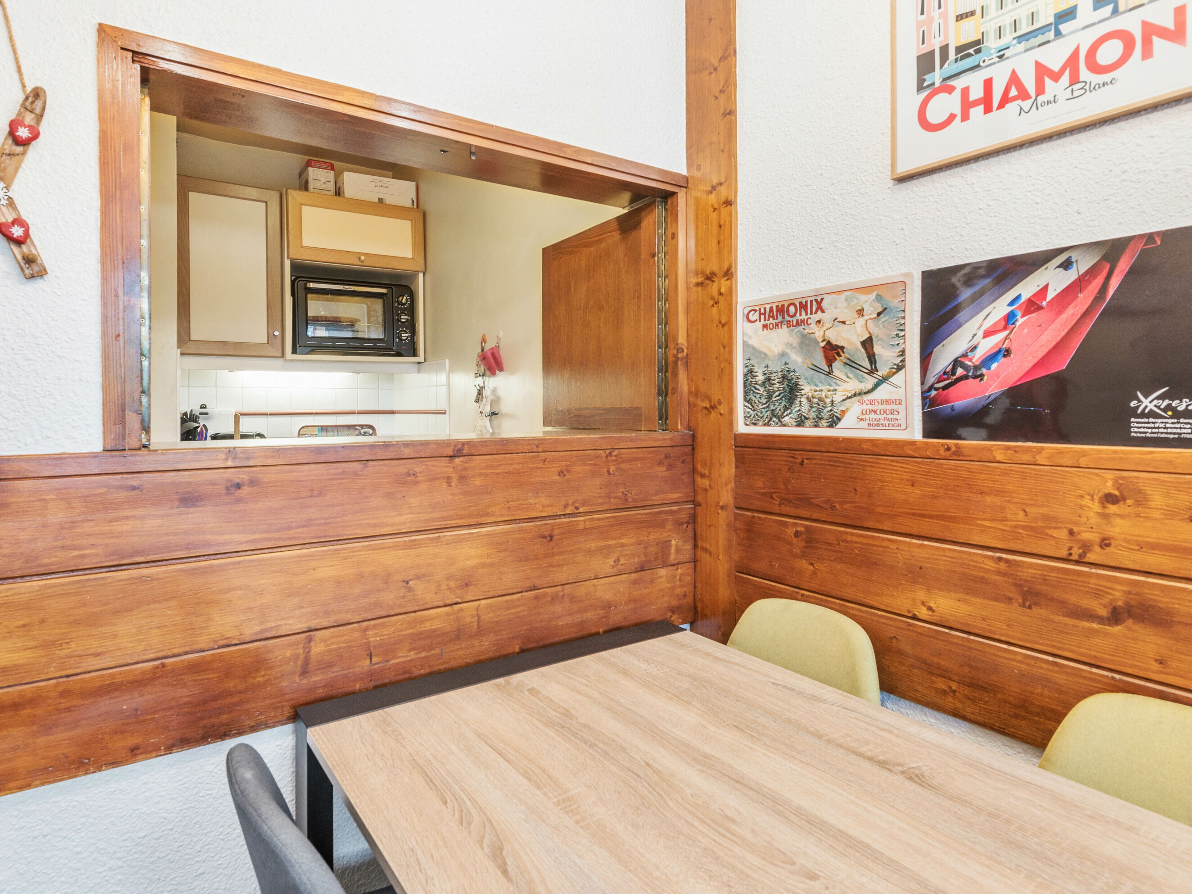 A wooden interior with a dining table, chairs, a kitchen area with cabinets, and a wall with a poster.