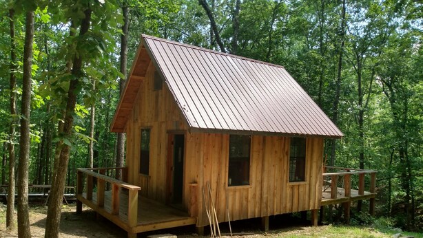 A wooden cabin with a metal roof, surrounded by trees. - Primitive Cabin in the woods. A place to unplug, unwind, and relax! (Parthenon)