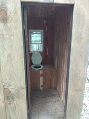 Een klein houten gebouwtje met één toilet en een raam.