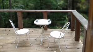 A wooden deck with two white metal tables and chairs, surrounded by a forest. - Primitive Cabin in the woods. A place to unplug, unwind, and relax! (Parthenon)