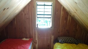 A small attic bedroom with wooden walls, a window, two beds with red and yellow bedding, and a wooden floor. - Primitive Cabin in the woods. A place to unplug, unwind, and relax! (Parthenon)