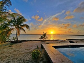 A pool area with a sunset view, palm trees, and a calm sea. - Grand Sunset Decks: Luxury Home on the Lagoon (Placencia)