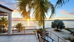 Una terraza con vistas al mar, palmeras y una puesta de sol.