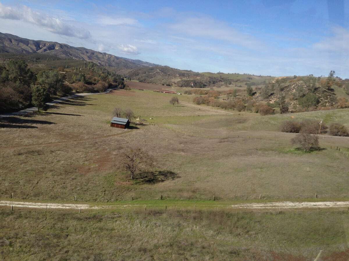 Un paysage rural avec un seul bâtiment, vraisemblablement une ferme, entouré de champs ouverts et de collines lointaines.