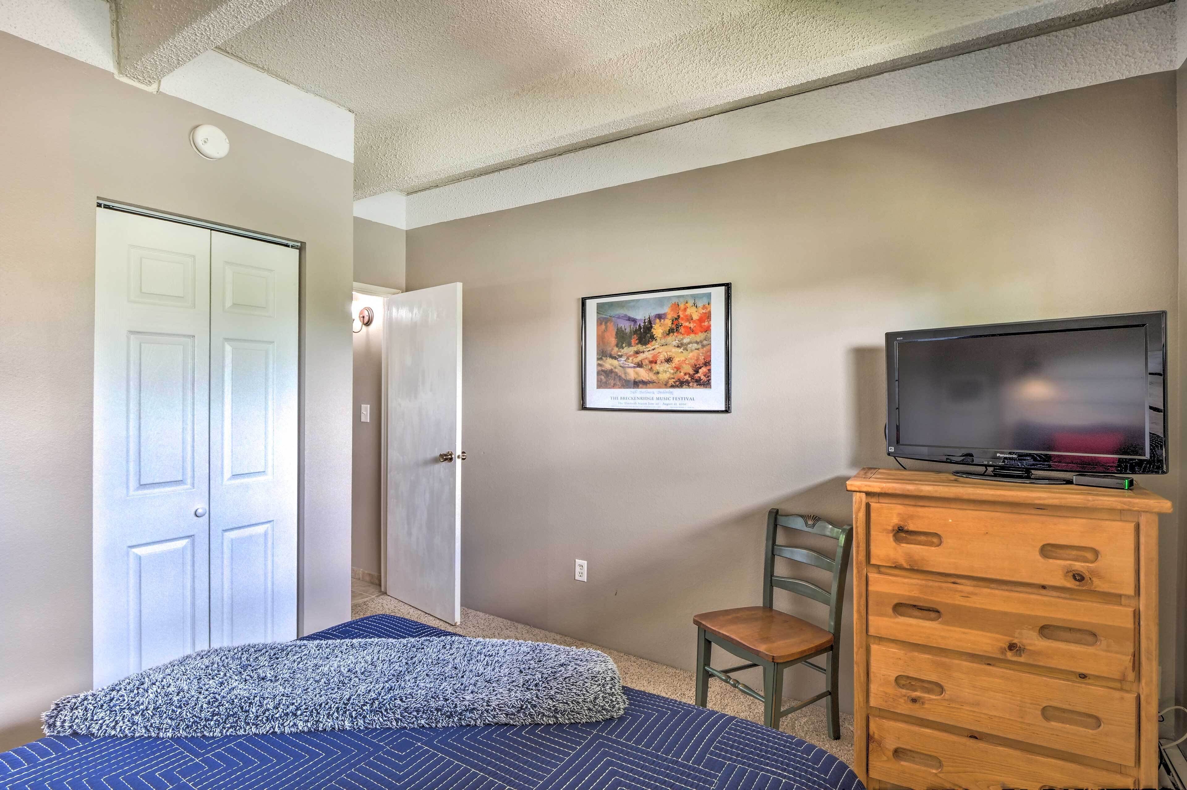 Une chambre à coucher comprenant un lit, une commode, un téléviseur, un tableau encadré accroché au mur et une porte donnant sur une autre pièce.