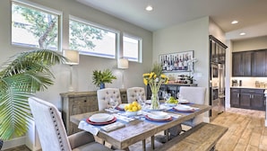 A dining area with a wooden table set for six, surrounded by upholstered chairs. There is a large window with a view of trees, a lamp, and a vase with flowers on the table. - Upscale Austin Area Escape: Families Welcome! (Austin)