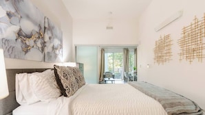 A bedroom with a bed, a nightstand, a lamp, a large abstract painting, and a view of the outdoors. - Beacon Hill 1BR - Rooftop + Patio - Near VA Medical - Monthly Stays (Seattle)