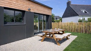 Ein modernes Haus mit Holzfassade, einer Schotterterrasse und einem Holztisch mit Kissen.