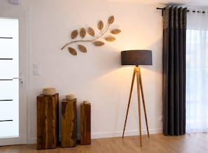 Ein Zimmer mit Holzboden, Wanddekoration in Form eines Blattes, einer Stehlampe und einer Tür mit horizontalen Linien.