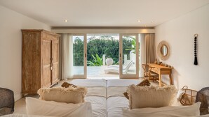 Une chambre dotée d’une grande porte-fenêtre coulissante donnant sur un balcon, d’une armoire en bois, d’un petit bureau en bois et d’un lit avec une literie blanche.