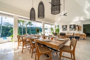 A spacious dining area with a long wooden table, wicker chairs, and hanging wicker light fixtures. - Sacred Jungle • Luxury 4BR Ubud • 2 Infinity Pools (Ubud)