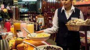 Disposição de buffet com diversos alimentos e um funcionário a servir.