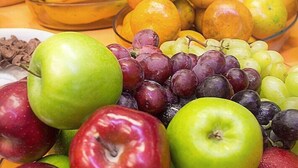 Uma tigela com maçãs, uvas, bananas e laranjas.